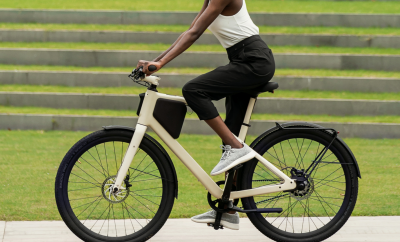 Femme roulant sur un vélo Lemmo One présenté de profil et de couleur crème