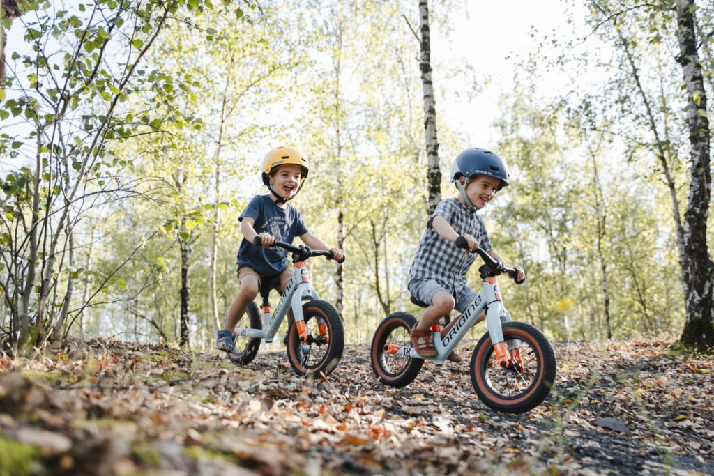 Deux enfants roulant sur draisienne Origine Cycles en forêt